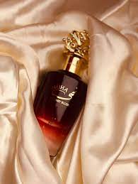 A dark glass perfume bottle with a gold ornate cap rests on smooth, cream-colored satin fabric.