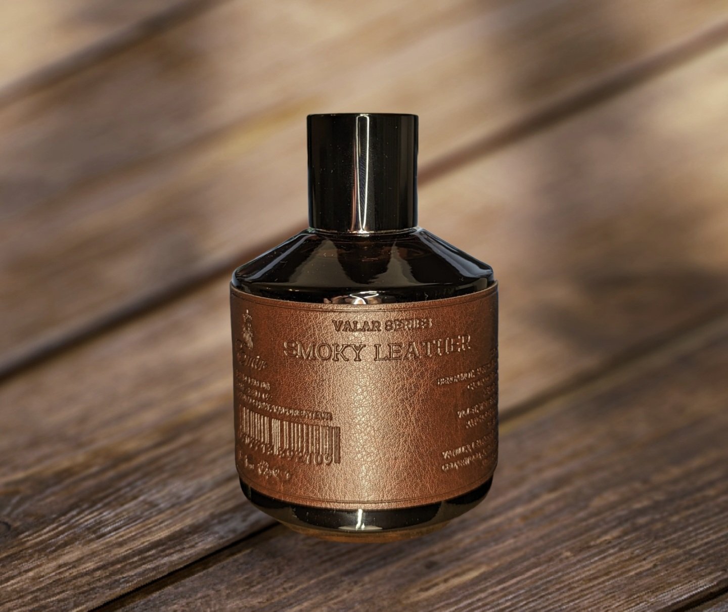A brown glass bottle of Paris Corner Emir Valar Series Smoky Leather 100ml Eau De Parfum, with a black cap and textured label, stands on wood—a refined fragrance from Paris Corner for bold scent enthusiasts.