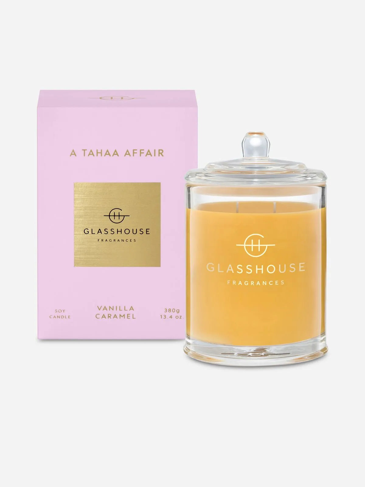 The Glasshouse A Tahaa Affair Soy Candle 380g features yellow soy wax in a glass jar and comes in a pink box, offering a sweet vanilla caramel scent.