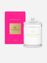 The Glasshouse Rendezvous Soy Candle 380g features elegant gold and black accents on both the candle with lid, labeled "Amber & Orchid," and its pink box, capturing the enchanting allure of amber.