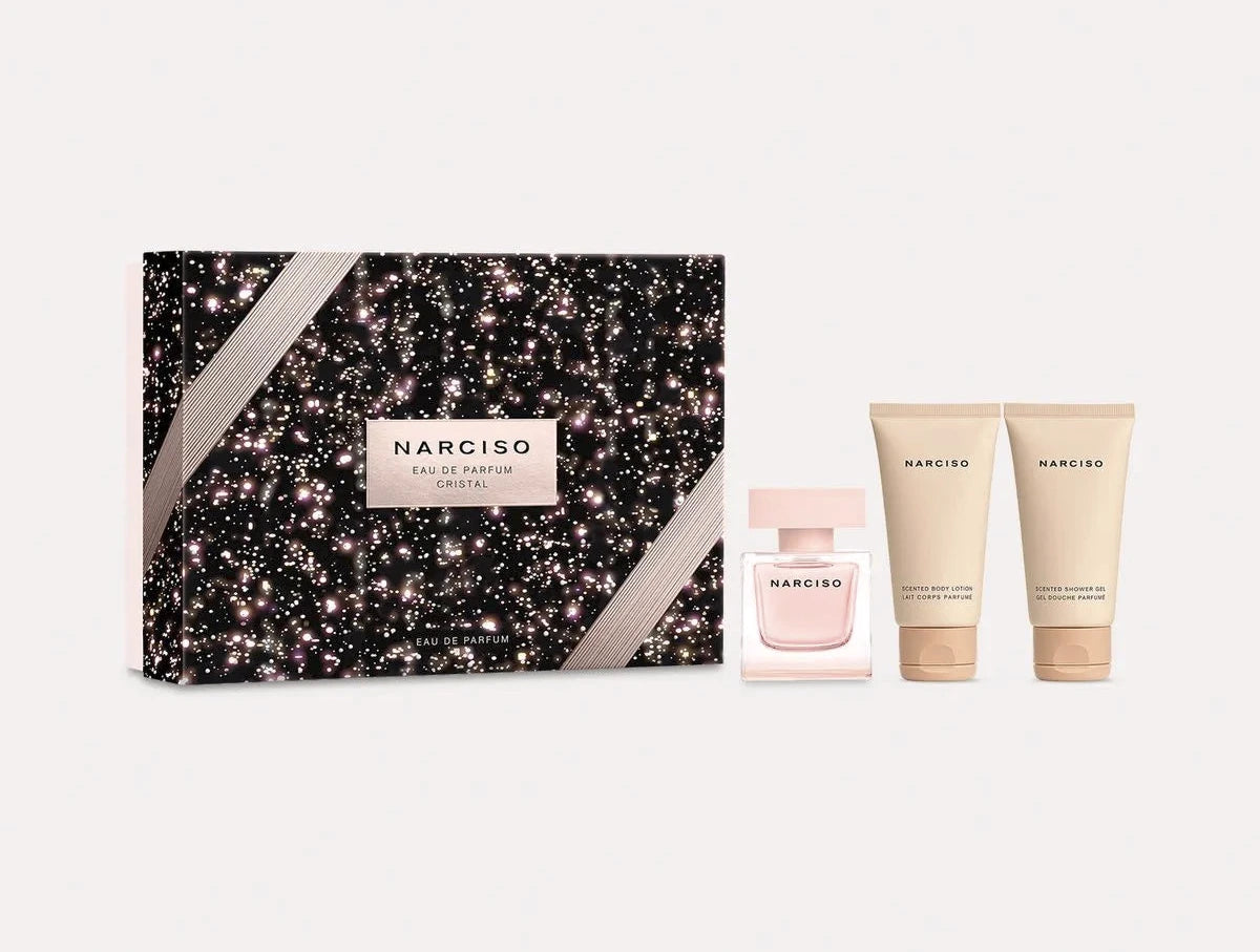 Narciso Rodriguez Cristal Eau de Parfum Gift Set by Narciso Rodriguez, featuring a black and pink sparkling box, an Eau de Parfum Cristal bottle, and two beige skincare tubes displayed on a white background.