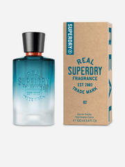 A Superdry Real 02 Masculine 100ml EDT bottle with a black cap is displayed beside its brown and blue cardboard packaging labeled “REAL SUPERDRY FRAGRANCE.” This aromatic fruity Eau de Toilette by Superdry embodies the essence of a contemporary men’s scent.