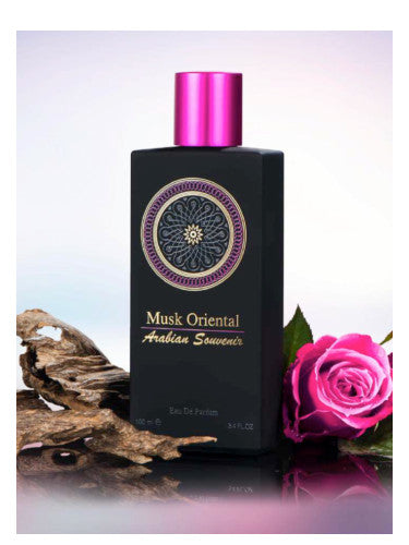Black perfume bottle labeled "AL Musbah Musk Oriental Arabian Souvenir" next to a pink rose and wooden bark, against a light purple background. (Rio Perfumes)