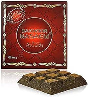 A box of Bakhoor Nabeel Nasaem Incense 40g by Rio Perfumes with an ornate red and gold design stands behind a segmented block of incense, evoking the rich aroma of fragrant woods within.