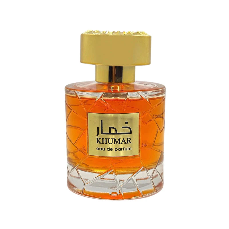 A clear glass bottle of Lattafa Khumar Sugar Wadi Al Khaleej 100ml EDP, filled with orange liquid and topped with a gold label and cap, offers an aromatic spicy unisex fragrance.