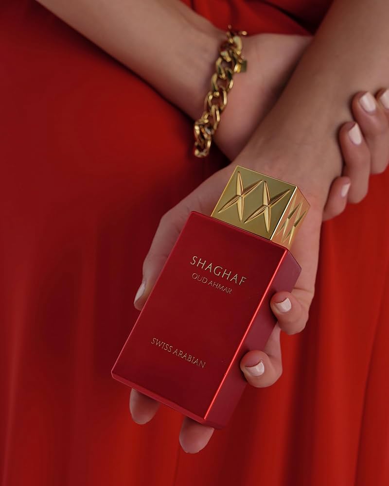 Load image into Gallery viewer, A woman in a red dress holding a Swiss Arabian Oud Ahmar 75ml Eau De Parfum bottle, exuding the captivating fragrance of this Swiss Arabian.

