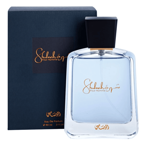 A rectangular bottle of Rasasi Shuhrah 90ml Eau De Parfum with light blue liquid, a black cap, and gold script next to its black packaging box displaying the same design. This sophisticated fragrance for men is an elegant addition to any collection.