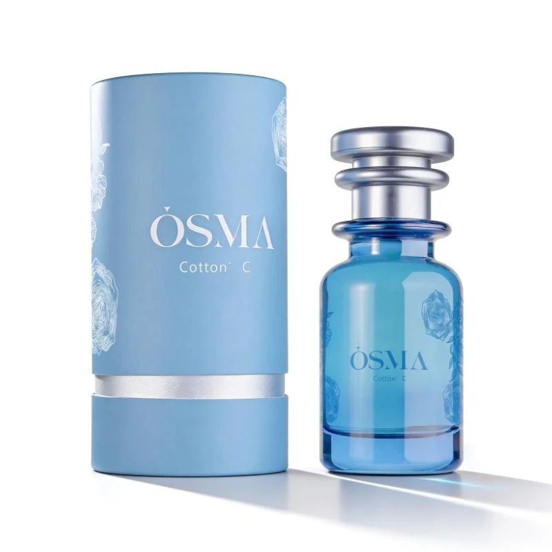 A blue cylindrical box labeled "Osma Perfumes Cotton C 75ml EDP" sits next to a matching blue glass bottle with a metallic cap, elegantly presenting this unisex fragrance featuring sandalwood oud notes.
