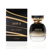 A perfume bottle labeled "Khadlaj La Fede Aura Kiss of Rose 100ml Eau De Parfum" is showcased next to its matching black and gold packaging. The clear bottle with a black top adorned in gold detailing embodies the essence of Eau de Parfum, delivering a captivating fragrance for men & women.