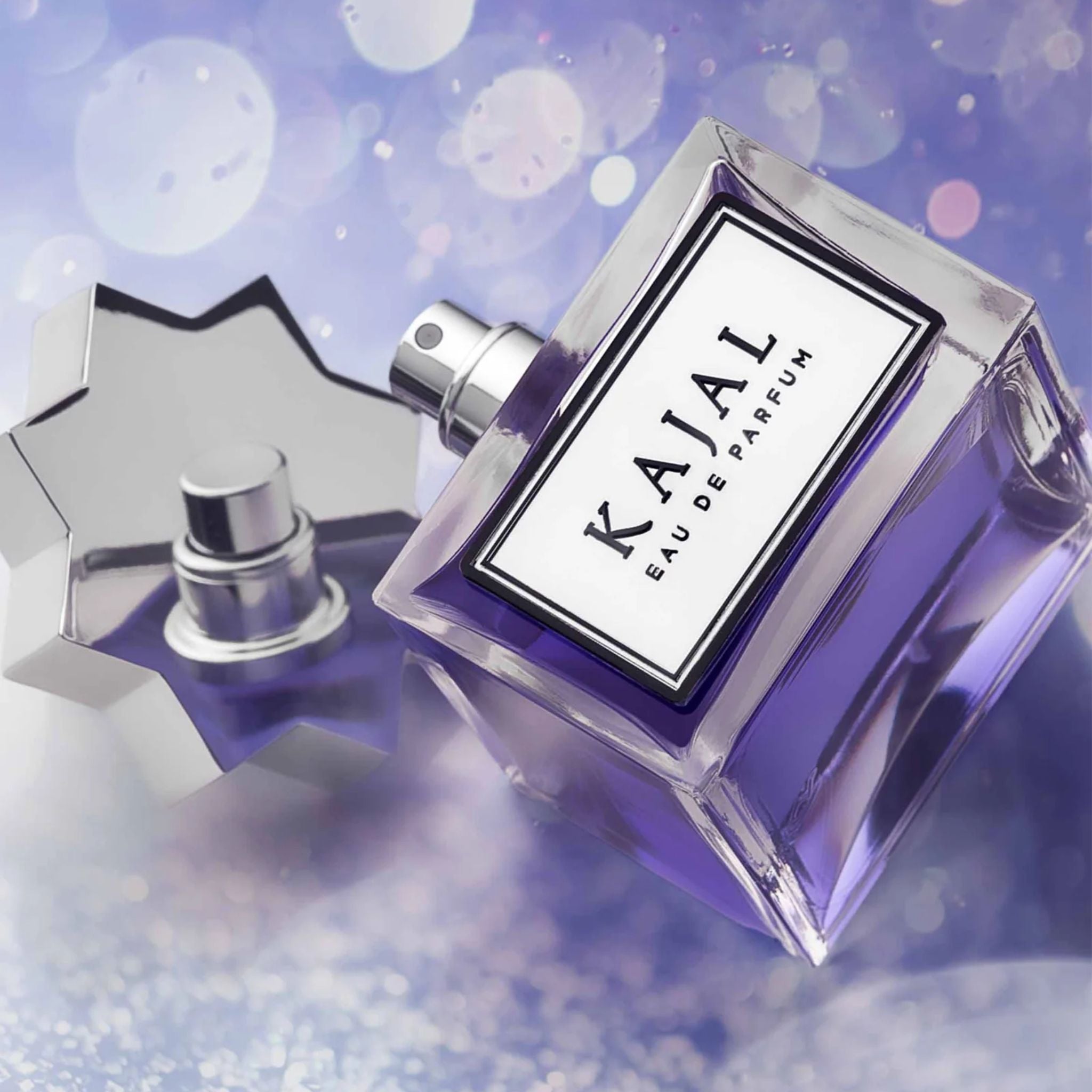 A square bottle of Kajal Eau de Parfum by Kajal, featuring purple liquid and a star-shaped silver cap beside it, is shown open against a blurred purple background.
