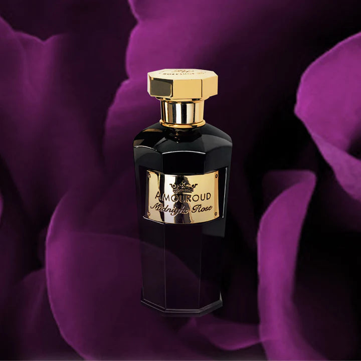 A dark, elegant bottle of Amouroud Midnight Rose Eau De Parfum features a gold cap and label, set against deep purple rose petals.