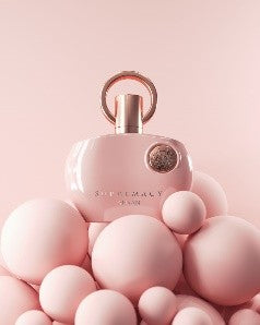 Afnan Supremacy Pink 100ml Eau De Parfum by Afnan, in a pink bottle with a round gold cap, is displayed among pink spheres of different sizes against a pink background.
