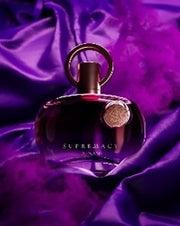 A bottle of Afnan Supremacy Purple 90ml EDP by Afnan rests on purple satin with swirls of purple smoke—a luxurious women's fragrance.
