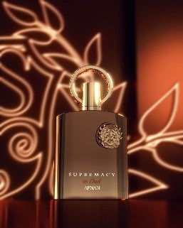 A bottle of Afnan Supremacy in Oud 100ml Extrait de Parfum by Afnan is displayed against a warmly lit background with abstract golden patterns, reflecting the perfume’s luxurious oud character.