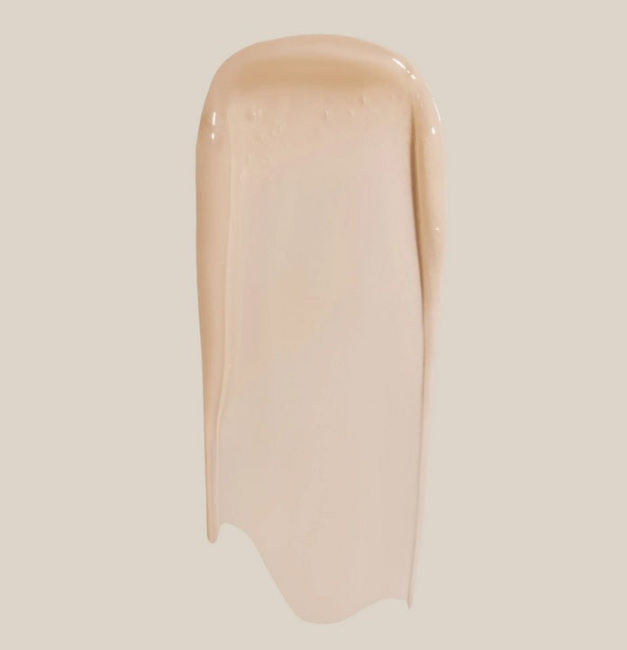 A beige liquid foundation swatch is spread smoothly on a light background, mirroring the creamy texture of Summer Fridays Lip Butter Balm Vanilla.
