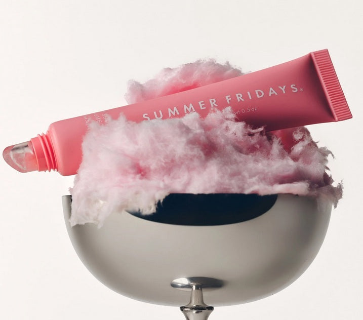 A tube of Summer Fridays Lip Butter Balm Pink Sugar by Summer Friday sits on fluffy pink cotton candy in a silver bowl, creating sweet pink sugar vibes against a neutral background.