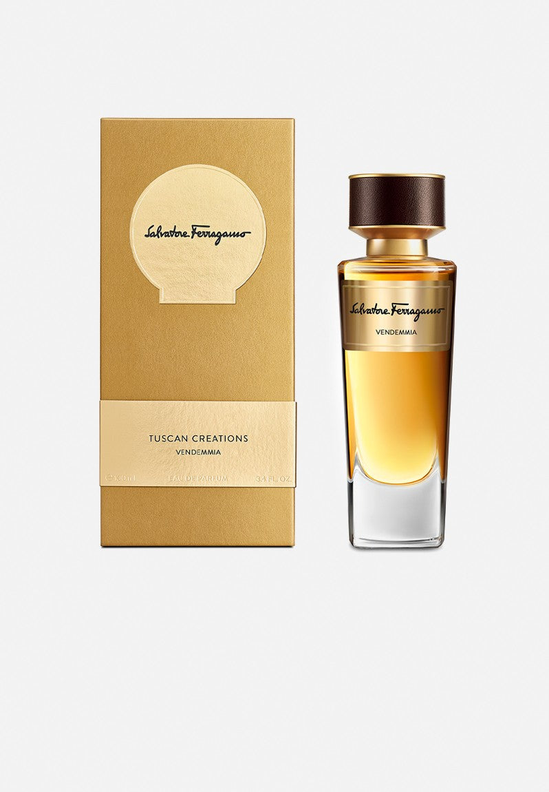 A gold box labeled "Salvatore Ferragamo Tuscan Creations Terra Rossa" stands next to a matching gold and brown perfume bottle filled with amber liquid—an elegant Tuscan perfume from Salvatore Ferragamo, available in 100ml EDP.