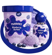 A bottle of Tubbies Tubbees Blueberry Sorbet EDP is displayed alongside a scoop of blueberry sorbet and fresh blueberries, all arranged neatly on a white surface.