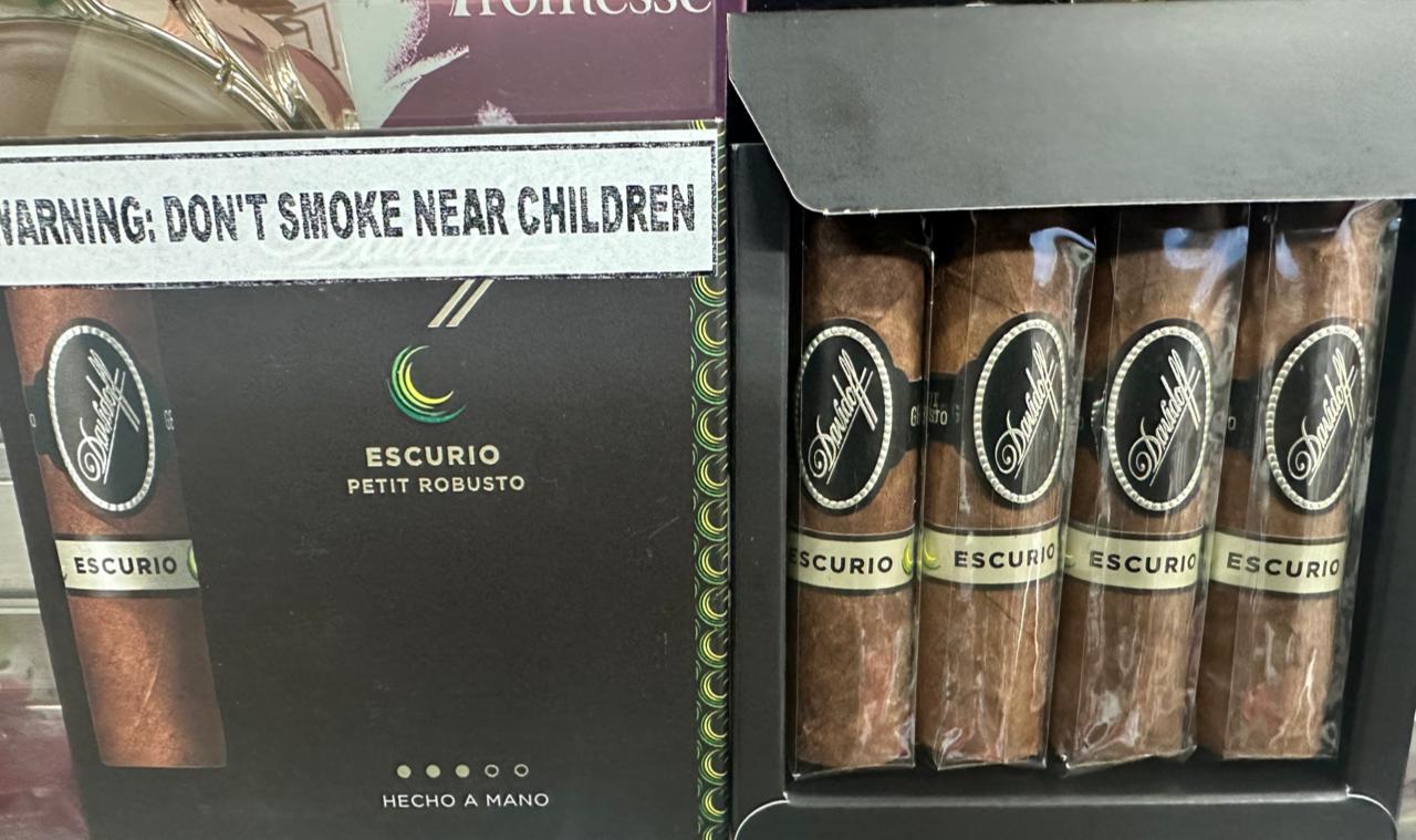 Image of Rio Perfumes Davidoff Escurio Petit Robusto 4 Pack Cigars in a box, displaying a warning "DON'T SMOKE NEAR CHILDREN." The cigars, made with Brazilian tobacco, have brown wrappers with labels, and the packaging mentions "HECHO A MANO.