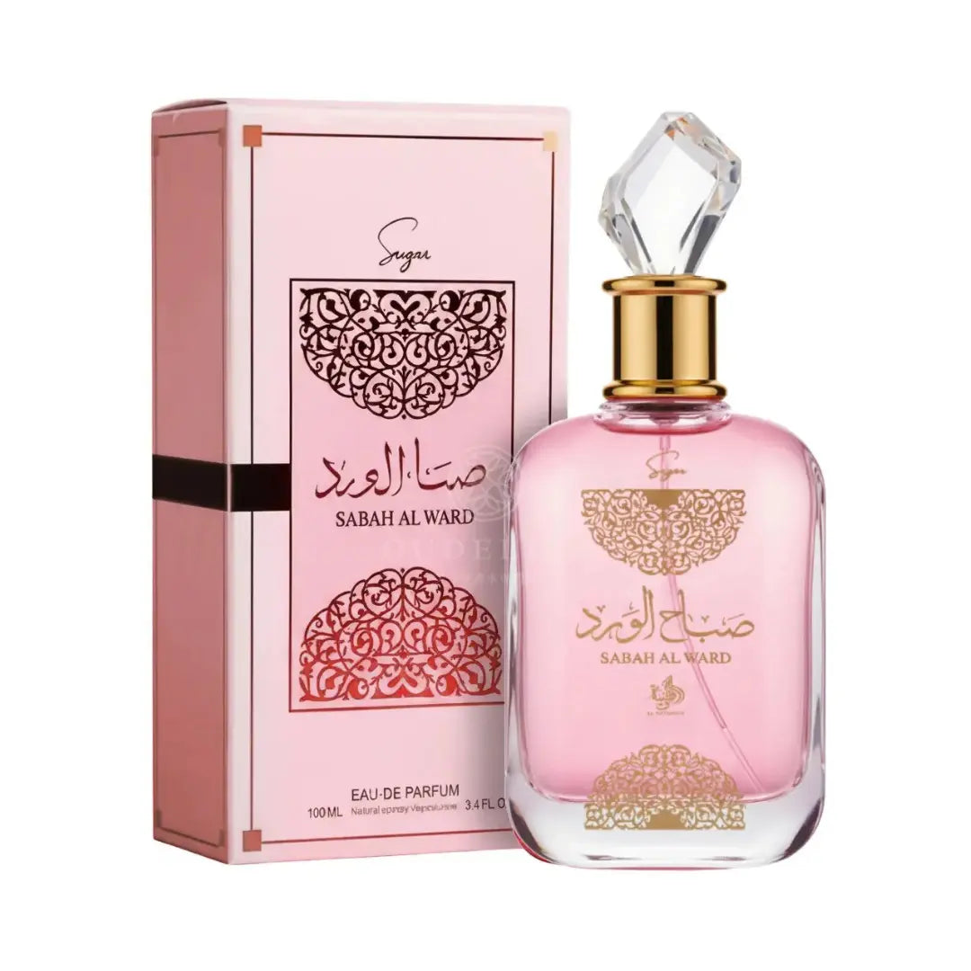 A pink perfume bottle adorned with gold accents and Arabic script stands beside a matching pink and gold box labeled "Sabah Al Ward Sugar." This Eau De Parfum, Al Wataniah Sabah Al Ward Sugar 100ml EDP by Al Wataniah, radiates Oriental Floral elegance—ideal for those who value luxurious scents and sophisticated design.