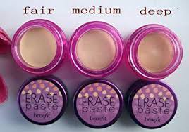 Three open containers of Benefit Erase Paste Conceal & Brighten by Benefit in fair, medium, and deep shades are shown, each with a matching labeled lid placed below.