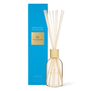 The Glasshouse Bora Bora Bungalow 250ml Diffuser by Rio Perfumes features a clear glass vessel with a gold cap, multiple reeds, and comes in a tall blue box. Enjoy an elegant home fragrance with teak and petitgrain notes.