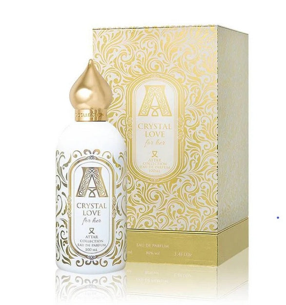 The Attar Collection's "Crystal Love for Her" 100ml Eau De Parfum bottle, featuring a white and gold design with a shimmering golden cap, stands beside its matching decorative box.