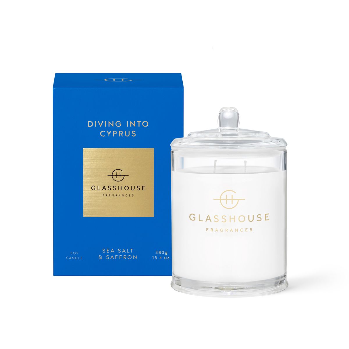 The Glasshouse Diving into Cyprus 380g Soy Candle, featuring sea salt and saffron notes, is displayed next to its blue and gold packaging—capturing the refreshing essence of Cyprus.