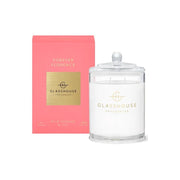 The Glasshouse Forever Florence 380g Soy Candle sits in a clear glass jar with a lid beside its pink and gold box, filling the air with the scent of wild peonies.