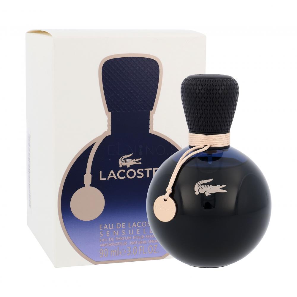 A round, dark Lacoste Eau De Lacoste Sensuelle 50ml Eau De Parfum bottle with a textured cap and tag sits in front of its matching box—a sophisticated women’s fragrance.