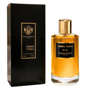 A 120ml bottle of Mancera Ombre Tonka Eau De Parfum by Mancera is displayed beside its elegant black and gold box. The bottle, filled with its signature amber-hued liquid, is crowned with a sleek gold cap.