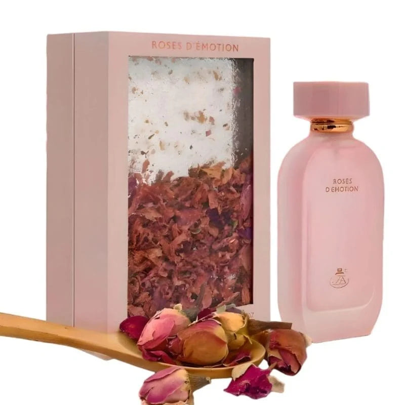 A pink bottle of Fragrance World Roses D’emotion 100ml EDP stands beside its box, surrounded by dried rose petals and a wooden spoon in the foreground, capturing the enchanting allure of an Arabian perfume by Fragrance World.