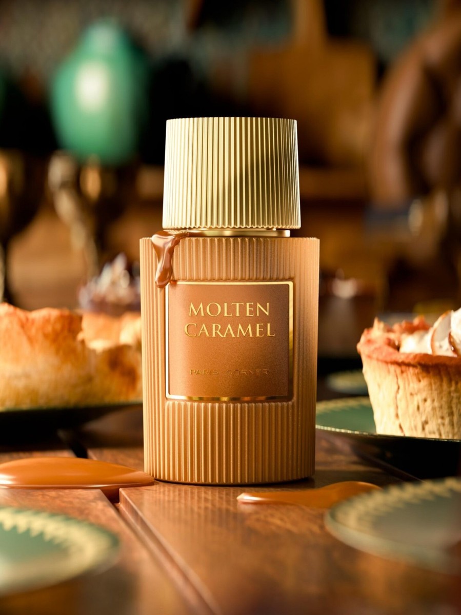 A 100ml bottle of Paris Corner Molten Caramel Eau De Parfum by Rio Perfumes sits on the table, its rich gourmand scent blending deliciously with the aroma of pastries and desserts.