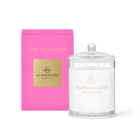 The Glasshouse Over the Rainbow Soy Candle 380g is shown in a clear glass jar with lid beside its pink and gold box, featuring soft, calming white musk notes.