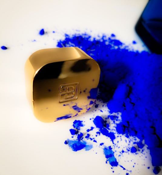 A blue powder and a bottle of Byron Parfums Mula Mula 75ml Extrait De Parfum Narcotic Collection on a white surface.