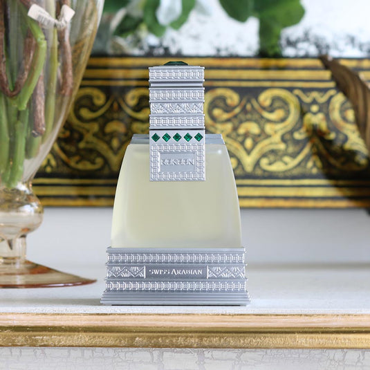 A bottle of Swiss Arabian Rakaan 50ml Eau De Parfum, with a fragrance for women, sits on a table next to a vase.
