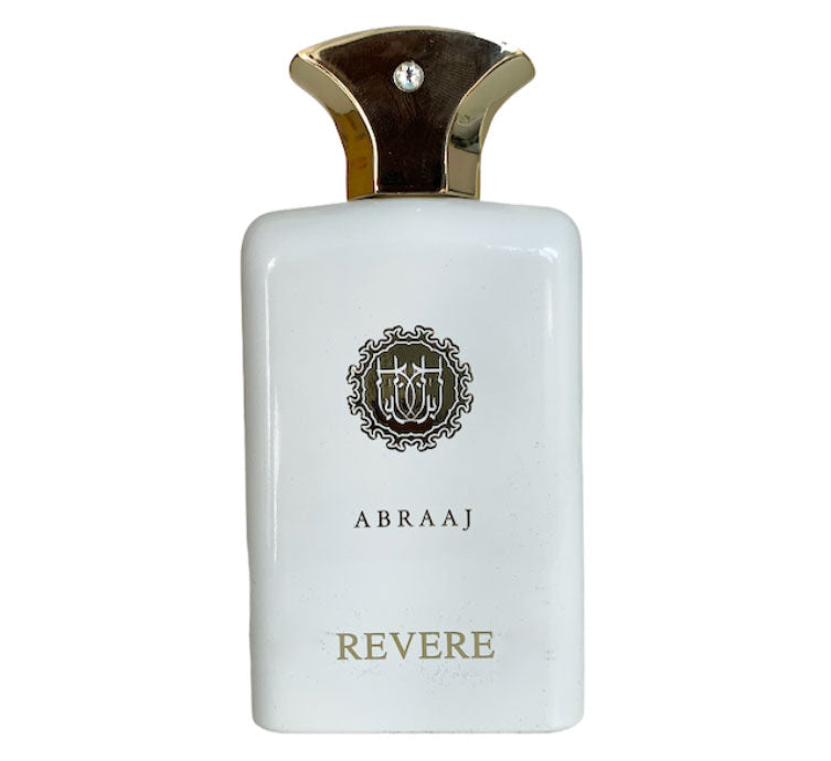A white bottle labeled "ABRAAJ REVERIE" with a gold and black cap and emblem, featuring the woody spicy scent of Paris Corner Abraaj Revere 100ml EDP by Paris Corner.