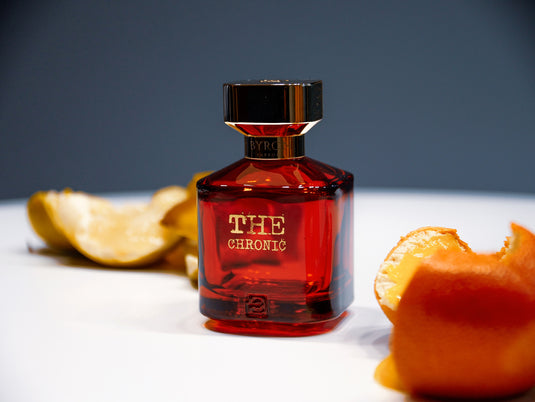 A bottle of Byron Parfums The Chronic 75ml Extrait De Parfum on a table next to a slice of orange.